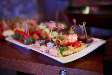 Snacks on the white plate. Canapes with cheese, shrimps, herbs, tomatoes and white bread in a nightclub.