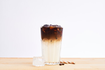 Iced coffee or latte macchiato in tall glass with straws on wooden table over white background. Copy space for text.