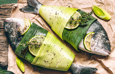 two fresh raw dorado fish, wrapped in palm leaves, sprinkled with a mixture of peppers and large...