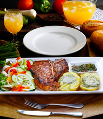 T bone steak with trimmings, potato, salad, orange juice, bread