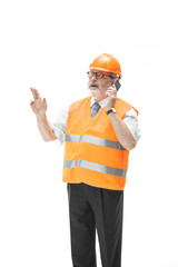 The builder in a construction vest and an orange helmet talking on a mobile phone about something. Safety specialist, engineer, industry, architecture, manager, occupation, businessman, job concept