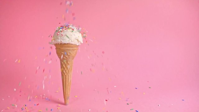 funny creative concept of wafer cone with ice cream covered and strewing sprinkles on pink background, copy space, slow motion