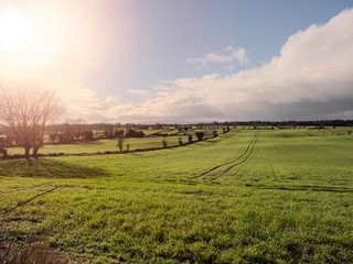 Fototapeta na wymiar Green sloped field, cloudy sky, sun flare. Ireland.
