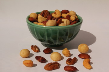 Fototapeta na wymiar Mixed nuts in a bowl with cashews, pecans, almonds and macadamias scattered on the table.