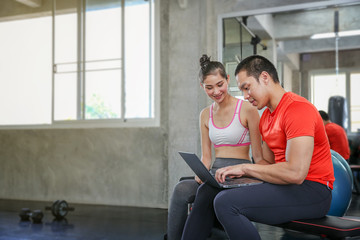 Women are discussing fitness with trainers. Young female talking during workout in gym. Female coach explaining directives with laptop or computer.