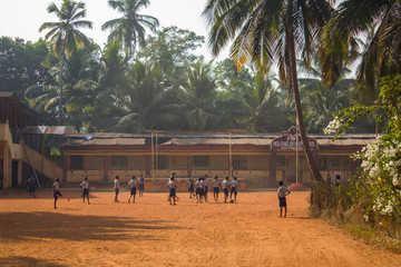 Querim, Goa/India - 10.01.2019: Indian schoolchildren boys and girls playing football barefoot in the school yard under green palm trees