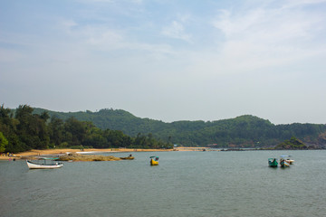 Fototapeta premium pleasure boats with tents on the sea near the shore against the background of a sandy beach and hills with a green forest, view from the ocean