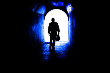 Person walking through tunnel towards light at end. Accomplishing goal or leaving darknenss for light.