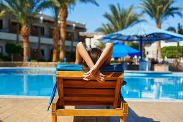 Woman in hat lying on a lounger near the swimming pool at the hotel, concept summer time to travel