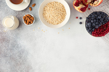 Healthy breakfast ingredients on grey concrete background, flatlay. Bowl of oat flakes with milk, fresh berries, nuts and fruits. Top view, copy space