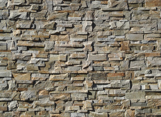Exterior wall cladding made of   natural stones with irregular shapes. Colors are shades of gray and brown 