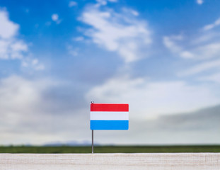 Flag of Luxembourg with vast meadow and blue sky behind it.