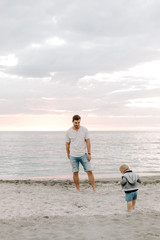 Adorably Perfect Young Father and Baby Toddler Son Family Having Fun Time at the Sandy Beach During Sunset Outside By the Ocean Water on Vacation