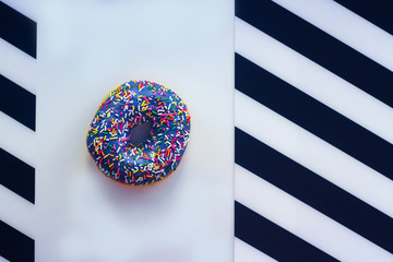 sweet Donut with icing and color dusting, on a white background with black and white stripes on the sides, top view.