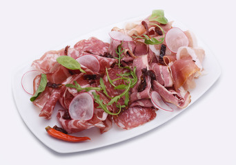 White plate with Thinly Sliced Salam sliced ​​ham, prosciutto with arugula leaves and radish on a white background