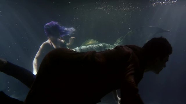fairytale mermaid and sunken man are floating inside ocean water near ground