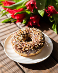 donut on white plate with tulips on a brown wooden background. Breakfast in summer time