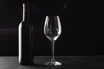 A bottle of red wine with a beautiful wine glass on a dark background