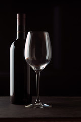 A bottle of red wine with a beautiful wine glass on a dark background