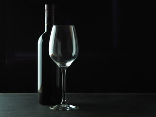 A bottle of red wine with a beautiful wine glass on a dark background