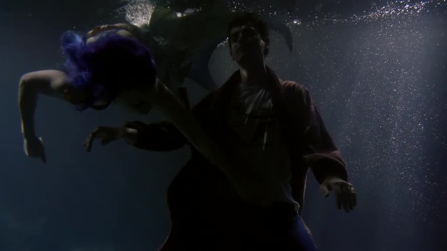 man is sinking underwater in ocean and magical mermaid woman is floating around him