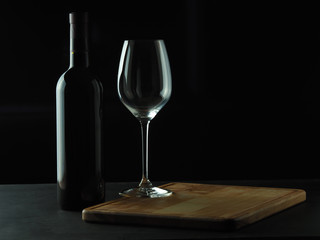 A bottle of red wine with a beautiful wine glass on a dark background