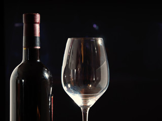 Red wine bottle and large wine glass over black background