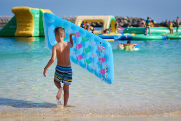 European boy with a colorful inflatable air mattress is enjoying his holidays on Canarias. He is...