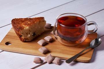 A piece of tasty pie, sweets and a cup of tea in a wooden cutting desk on the white background.