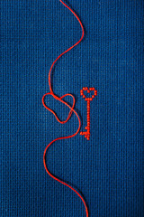 The red key from the heart is embroidered with red threads on a blue fabric.