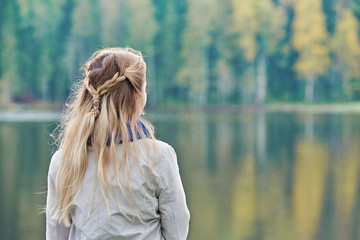 Young beautiful European woman is standing on the river bank and enjoying the wonderful view.