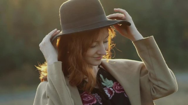 Charming red-haired girl with smile on face puts hat on head and looks aside