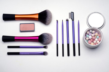Pattern of make-up brushes, blush and face powder on a white surface. Top view of women beauty...