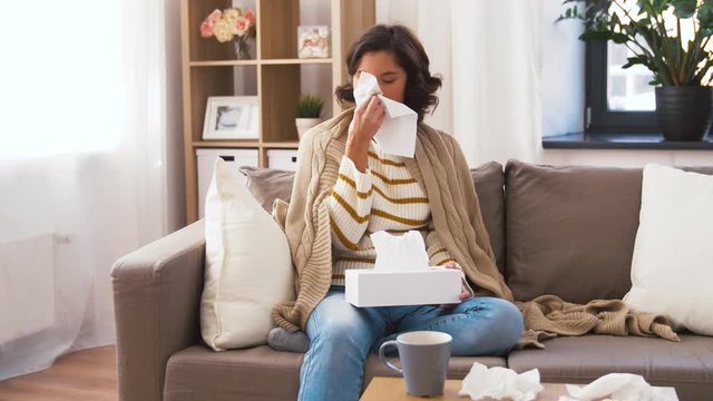 healthcare, cold, hygiene and people concept - sick woman in blanket taking paper tissue from box and blowing her nose at home