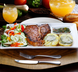 T bone steak with trimmings, potato, salad, orange juice, bread
