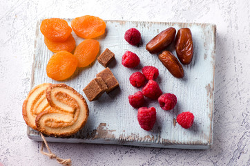 Raspberries, dates, dried apricots, cane sugar and cookies on a wooden board. Delicious and healthy vegetarian dessert