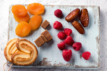 Fototapeta premium Raspberries, dates, dried apricots, cane sugar and cookies on a wooden board. Delicious and healthy vegetarian dessert