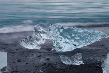 Amazing transparent blue iceberg pieces on Diamond beach with black sand near Jokulsarlon lagoon, Iceland. Ice calving. Water long exposure.