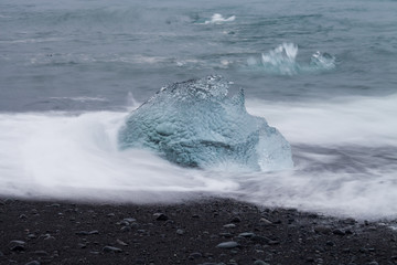 Naklejka premium Amazing transparent blue iceberg pieces on Diamond beach with black sand near Jokulsarlon lagoon, Iceland. Ice calving. Water long exposure.