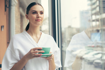 Beautiful woman enjoying her tea while standing near the window