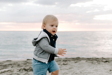 Fototapeta na wymiar Portrait of Cute Little Baby Boy Child Playing and Exploring in the Sand at the Beach During Sunset Outside on Vacation in Hoodie Zip-Up Sweat Shirt