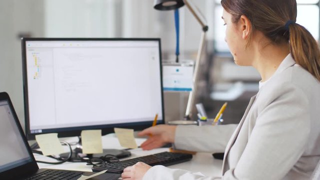 business, programming and technology concept - female programmer with notebook, sticky notes and computer working at office