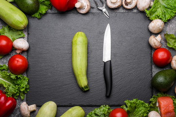 Frame made with raw vegetables and kitchen utensils. Knife and zucchini on a shale board