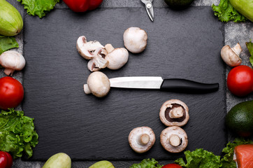 Frame made with raw vegetables and kitchen utensils. Knife and mushrooms on a shale board