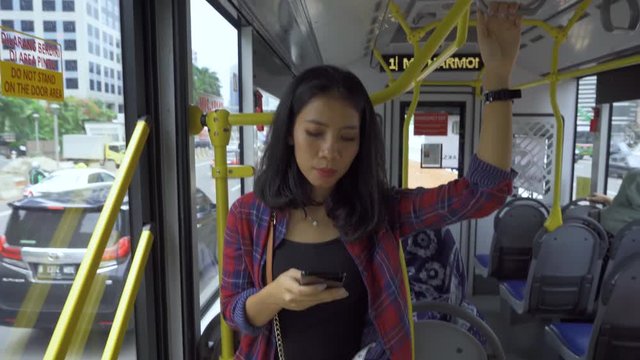 JAKARTA, Indonesia - March 21, 2019: Young Asian woman using smartphone while standing in the Transjakarta bus. Shot in 4k resolution