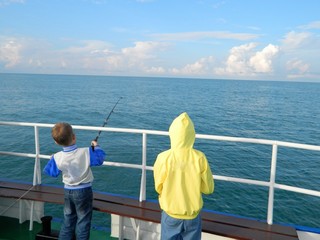 Fototapeta premium Children enthusiastically catch fish from a boat on sea fishing. Quiet early morning. 