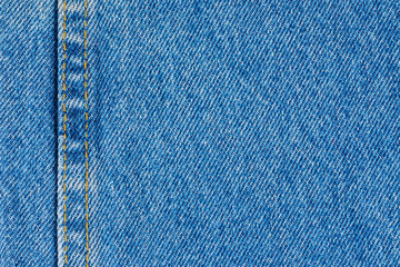Jeans background denim pattern with yellow seam. Classic blue stonewashed fabric texture. Background of jeans canvas close up.