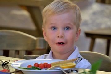  surprised boy sits at a table in front of a plate of food