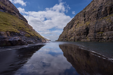 Black sand beach during low tide period between high rocky mountains close to seashore in village Saksun in Faroese island Streymoy in North Atlantic during sunny spring day, blue sky with clouds. © jdmfoto