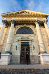 Obraz premium Young woman is standing by the Main entrance to Szechenyi thermal bath lit by the evening sun in BudaPest, Hungary